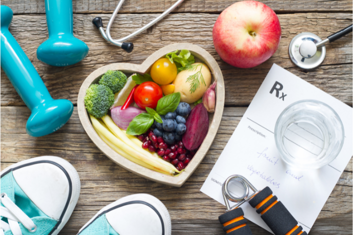 Healthy Fruits in a heart-shaped bowl, hand weights, sneakers, apple, stethoscope and Rx to eat fruit and vegetables