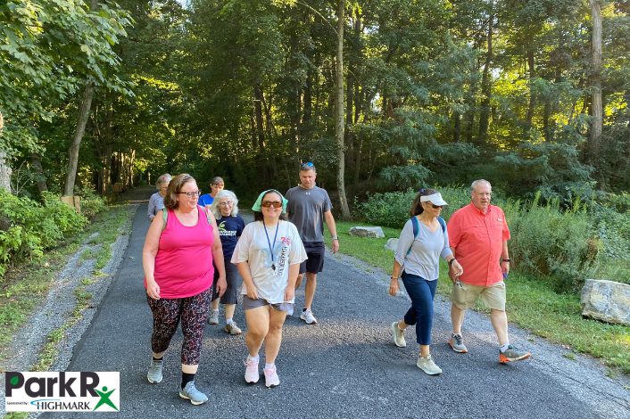 A group of people walking on a paved trail in the woods