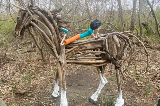 Horse made from tree branches with a child on it's back also made from natural materials
