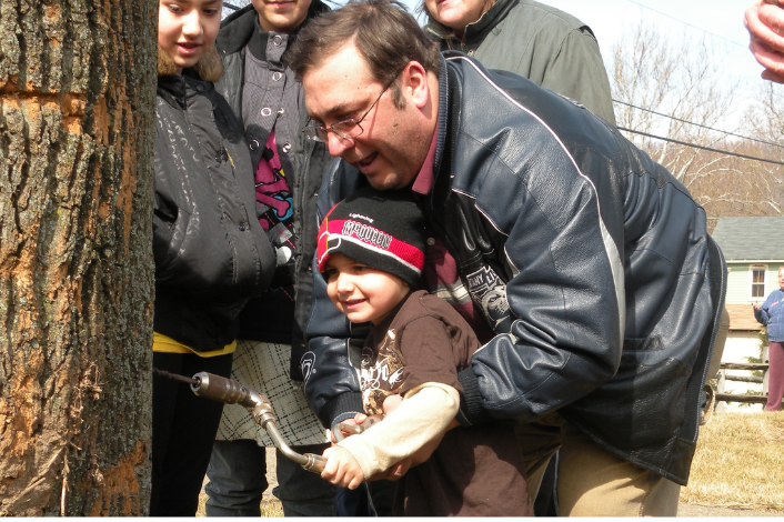 A man with a child tapping a tree for maple syrup