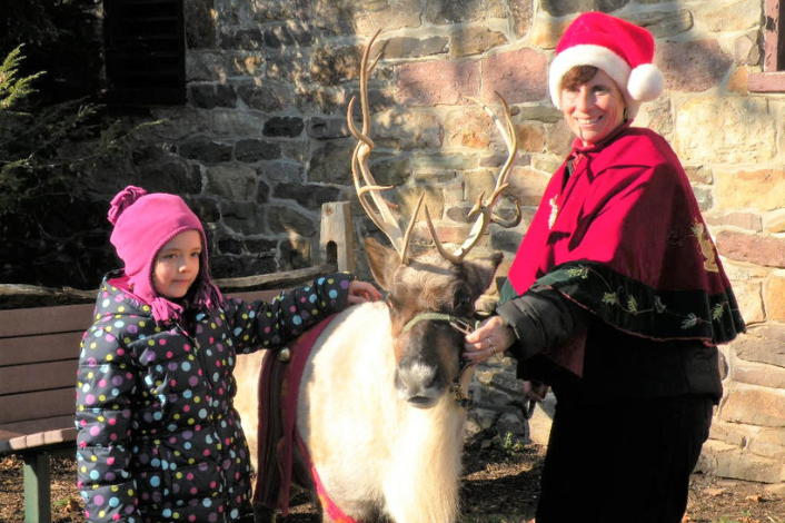 Child standing beside a live reindeer with Mrs. Claus