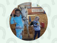 Child smiling while standing beside a miniature horse.