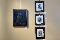 4 pieces of artwork featuring a raccoon, birds and birds nest with eggs hung on a tan wall