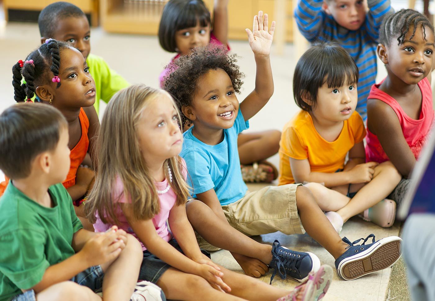 Young children sitting on the floor listening intently to an adult reading a story